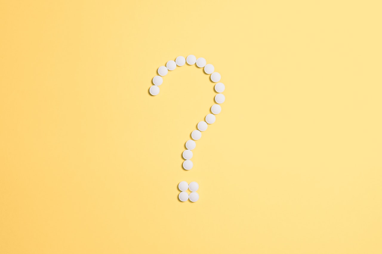 Several white pills on a yellow background, arranged into the shape of a question mark.