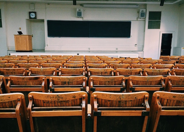 A large empty lecture hall with wooden chairs and a chalkboard in the front