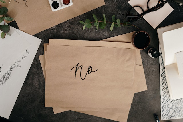 a neat desk with a stack of brown papers, the top paper has the word "no" written on it nicely
