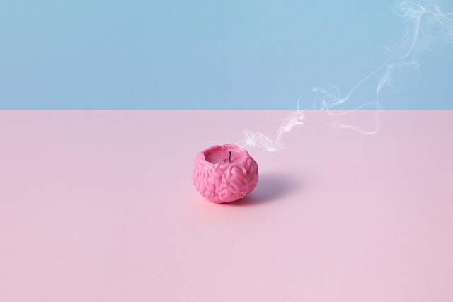 Brain candle with blue and pink background. the candle has been blown out and there is smoke