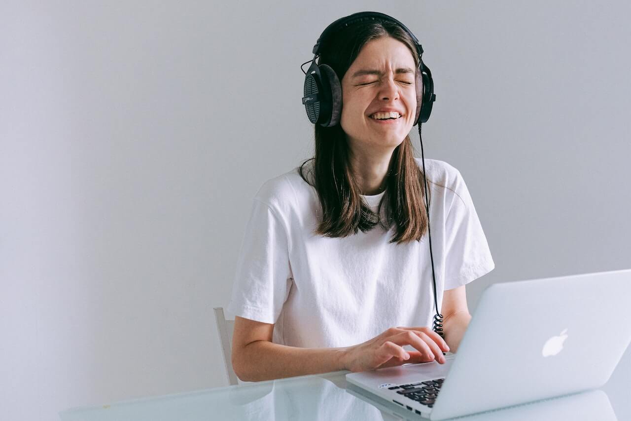 An image of a woman in a white shirt sitting at her computer with headphones on and crying.