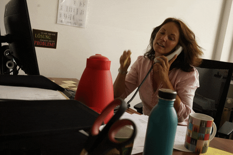  A woman with ADHD at her desk trying to organize her phone, coffee mug, and notes