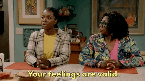 A gif of two Black women sitting next to each other at a table in a living/dining space. The one on the left is saying to somebody who is off-screen: Your feelings are valid. while emphasizing her message by gesturing with her hands. The woman to her right is looking at her, then turns toward the person off-screen while nodding approvingly, affirming the other woman's statement.