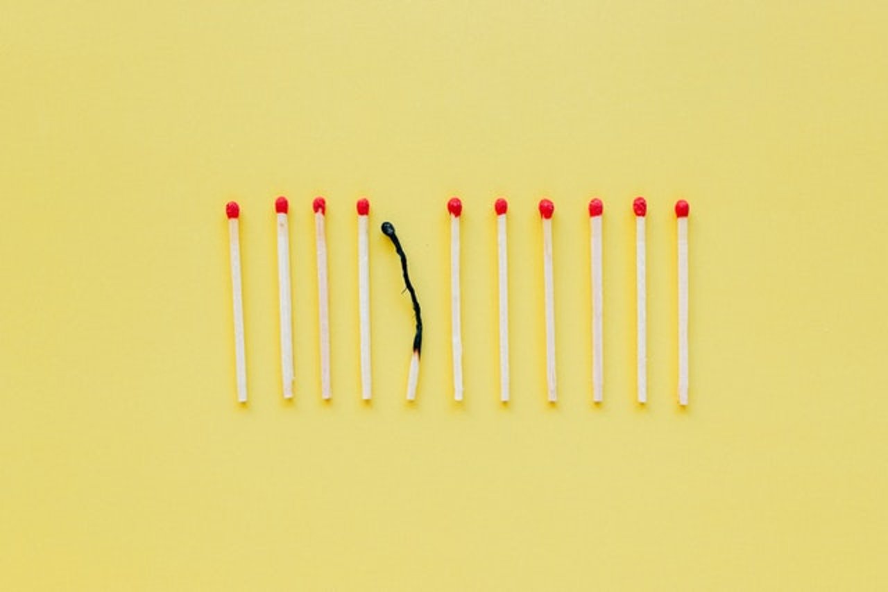 a yellow background with matches on top. One is very burnt while the rest are untouched