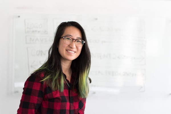 A woman smiling in a black and red plaid t shirt with glasses on