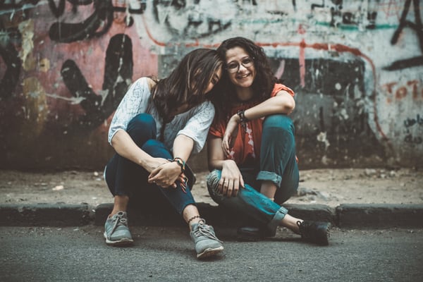 two women sitting next to each other on a curb and laughing.