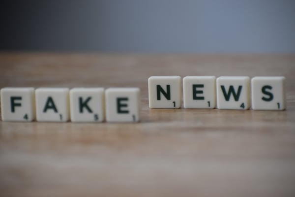 letter game pieces that are on a table and spell out "fake news"