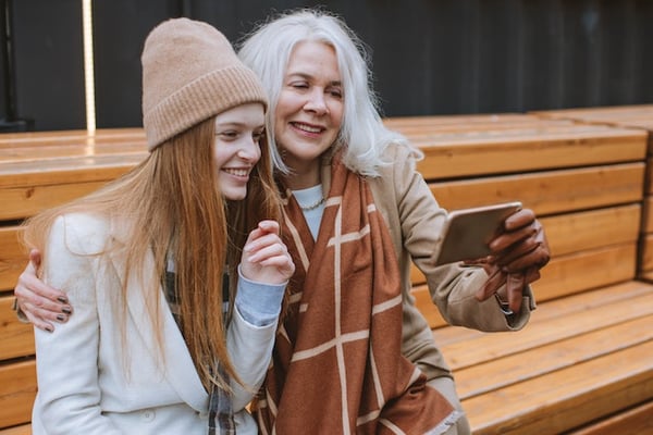 two women at different ages, sitting on a bench and holding a phone
