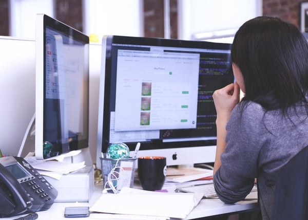 A woman sitting at an office desk with multiple screens in front of her.