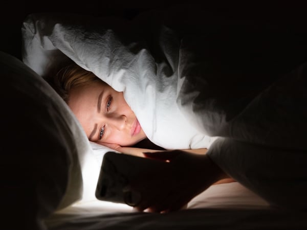 Woman reading on her phone under the duvet.