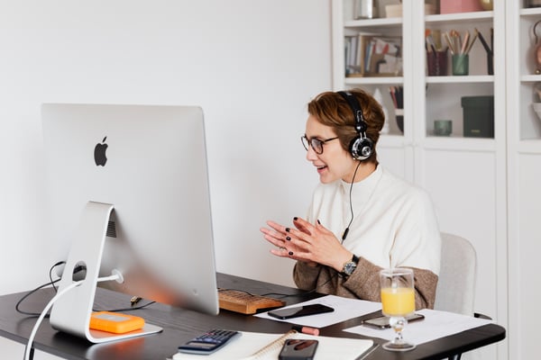 woman with short hair sitting at the computer with headphones on, having a meeting with someone.