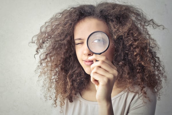 girl with long curly hair holding a magnifying glass