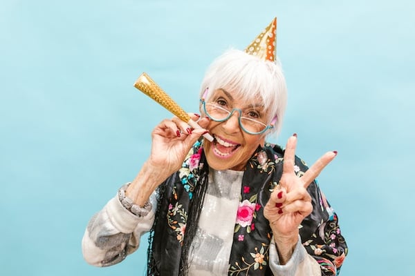 An old woman with adhd and a party hat on, smiling and laughing