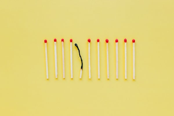 a yellow background with matches on top. One is very burnt while the rest are untouched
