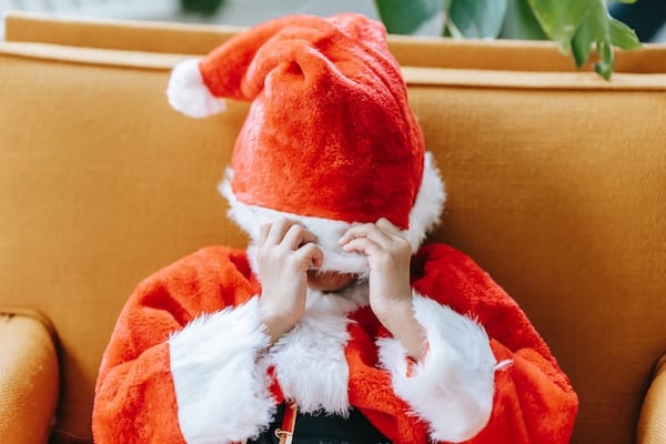 How to manage ADHD overwhelm during the holidays. A kid in a Santa Claus suit with the hat pulled down over their face.