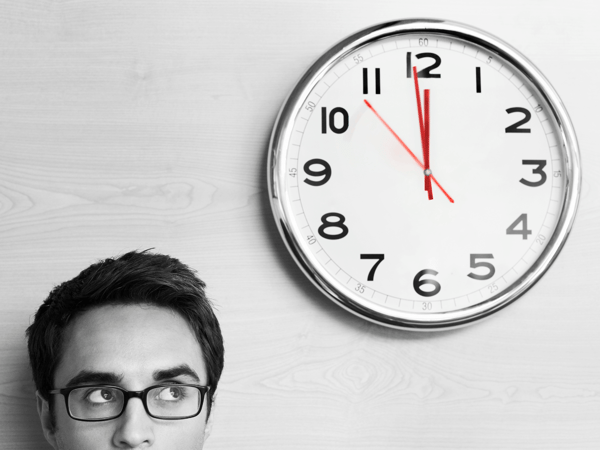 Feeling like you're wasting your time is a common experience among ADHDers who have time anxiety. Image shows a man in the corner looking anxiously up at the wall clock.