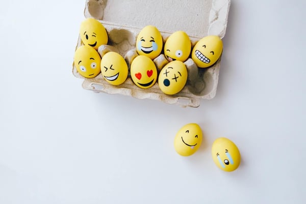 a carton of painted eggs, all of which are expressing different ranges of emotions that are drawn on them