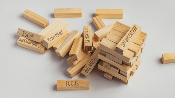 Jenga tower blocks that have fallen over. Some of the blocks have words on them: social awkwardness, movement, focus, balance, sensory, and organization.