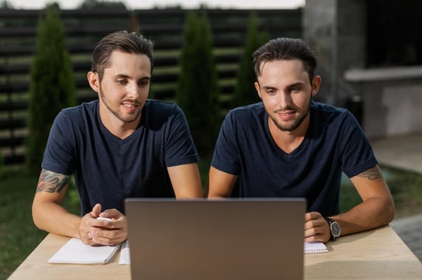 Twin brothers sit in front of a laptop to represent virtual body doubling.