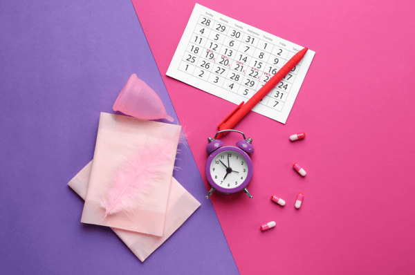 An image showing a calendar, alarm clock, and sanitary items for a menstrual cycle.