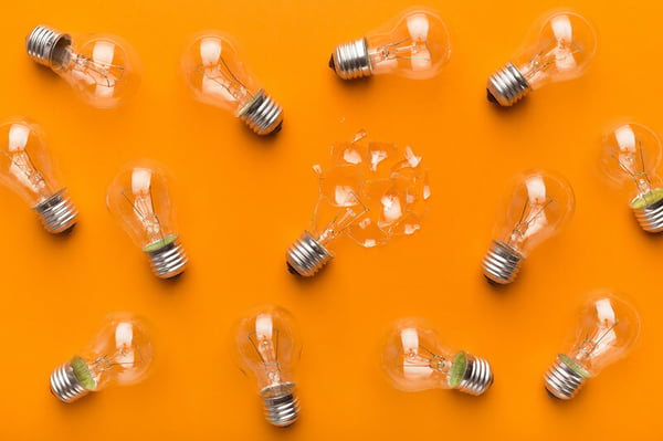 Glass lightbulbs sit on an orange background. One of the bulbs is broken.