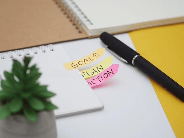 Blank notepad with bright color sticky note flags reading "goals," "plan," and "action."