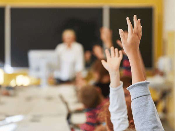 Teenage students with ADHD raising their hands in a classroom.