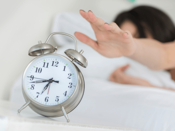 woman reaching forward to snooze her alarm clock