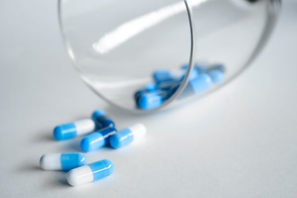 a glass spilling out blue and white pill capsules