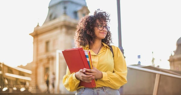 College student standing on campus, smiling and holding a book and binder