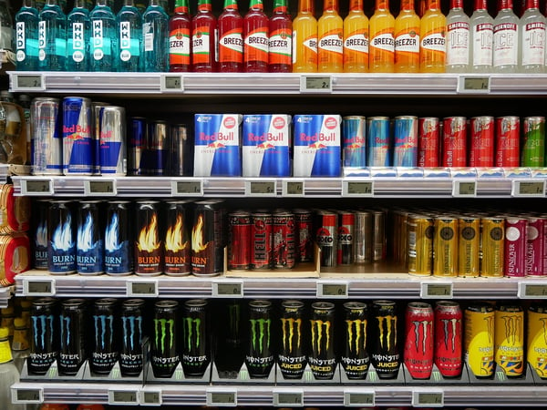 A fully-stocked store shelf with colorful cans of energy drinks popular among people with ADHD, including several types of Monster and Red Bull cans.