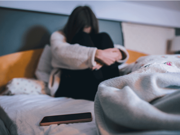 A woman with phone anxiety and ADHD sits on her bed frozen and hiding from her mobile phone.