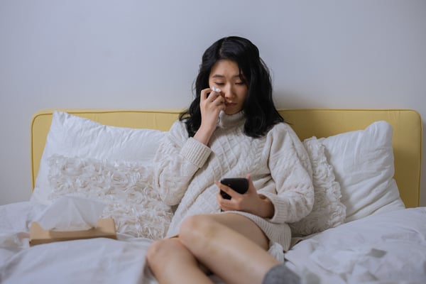 woman sitting on her bed and looking at her phone, crying because of rejection sensitive dysphoria