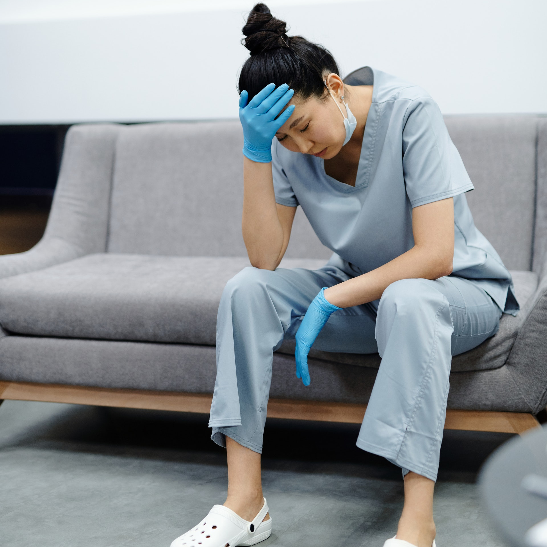 an asian woman nurse or doctor leaning forward on a chair with her head in her hand. She appears to be sleeping or exhausted.