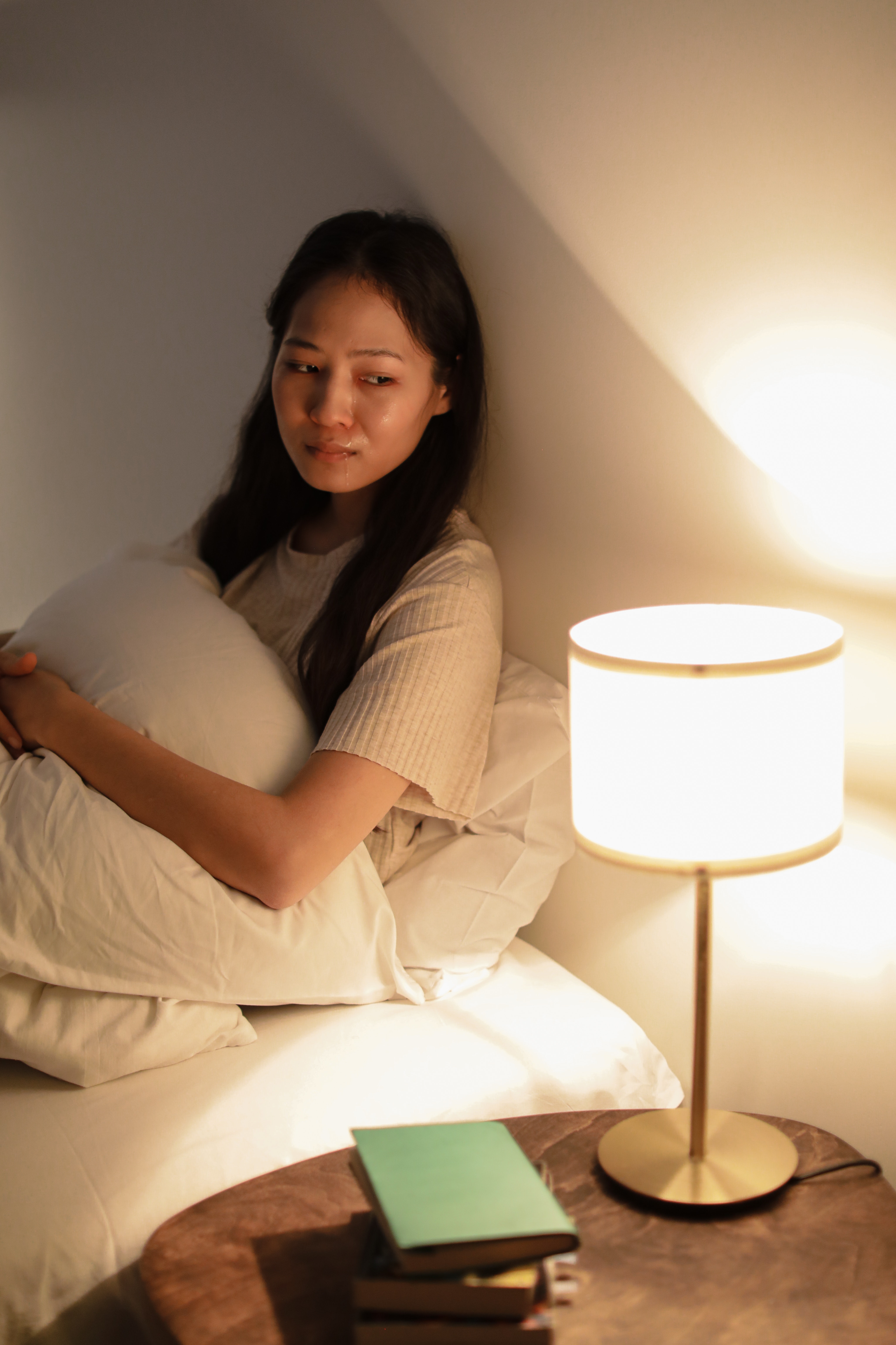 an asian woman sitting up in bed with tears streaming down her face