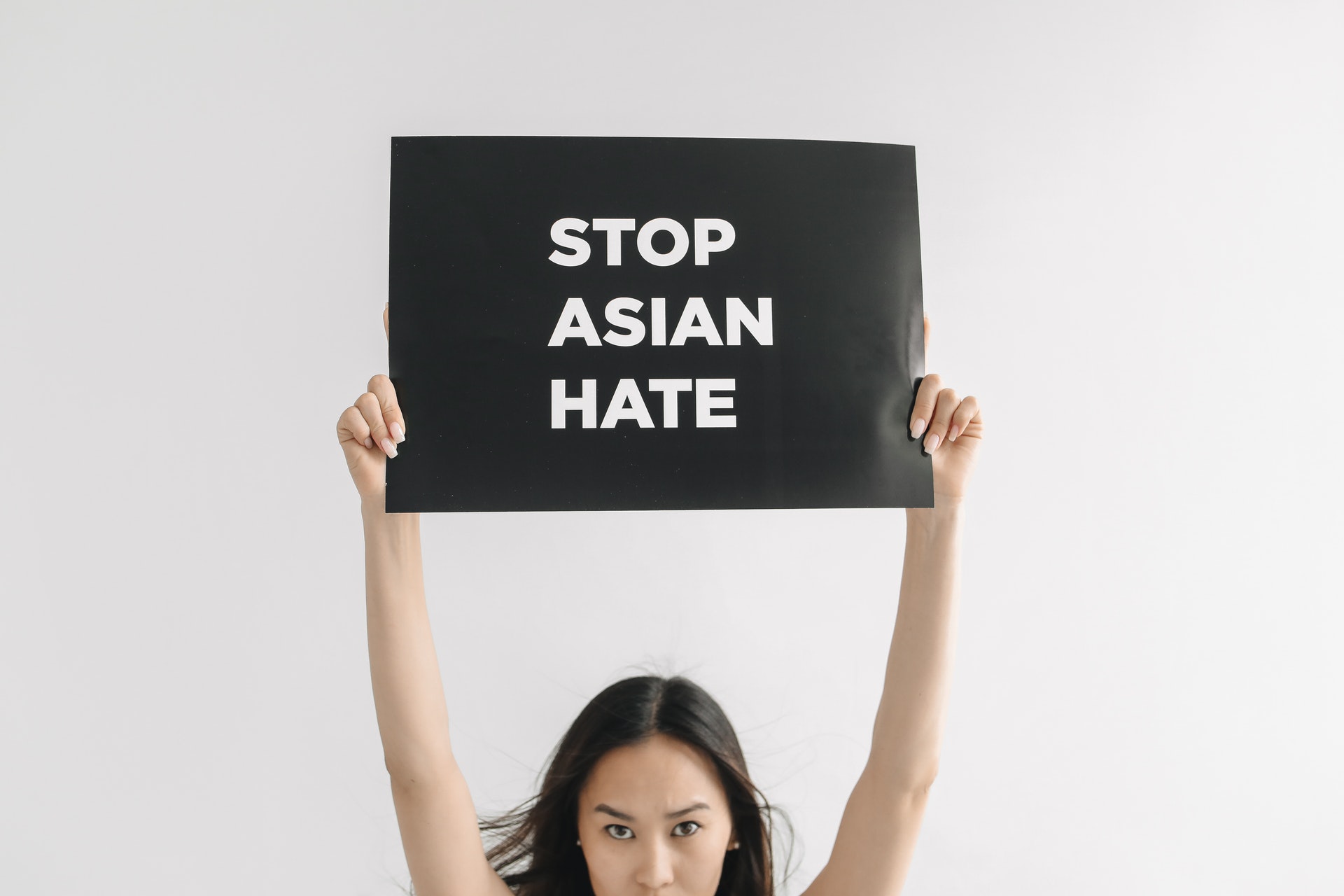 an asian woman holding up a black sign with white lettering: stop asian hate