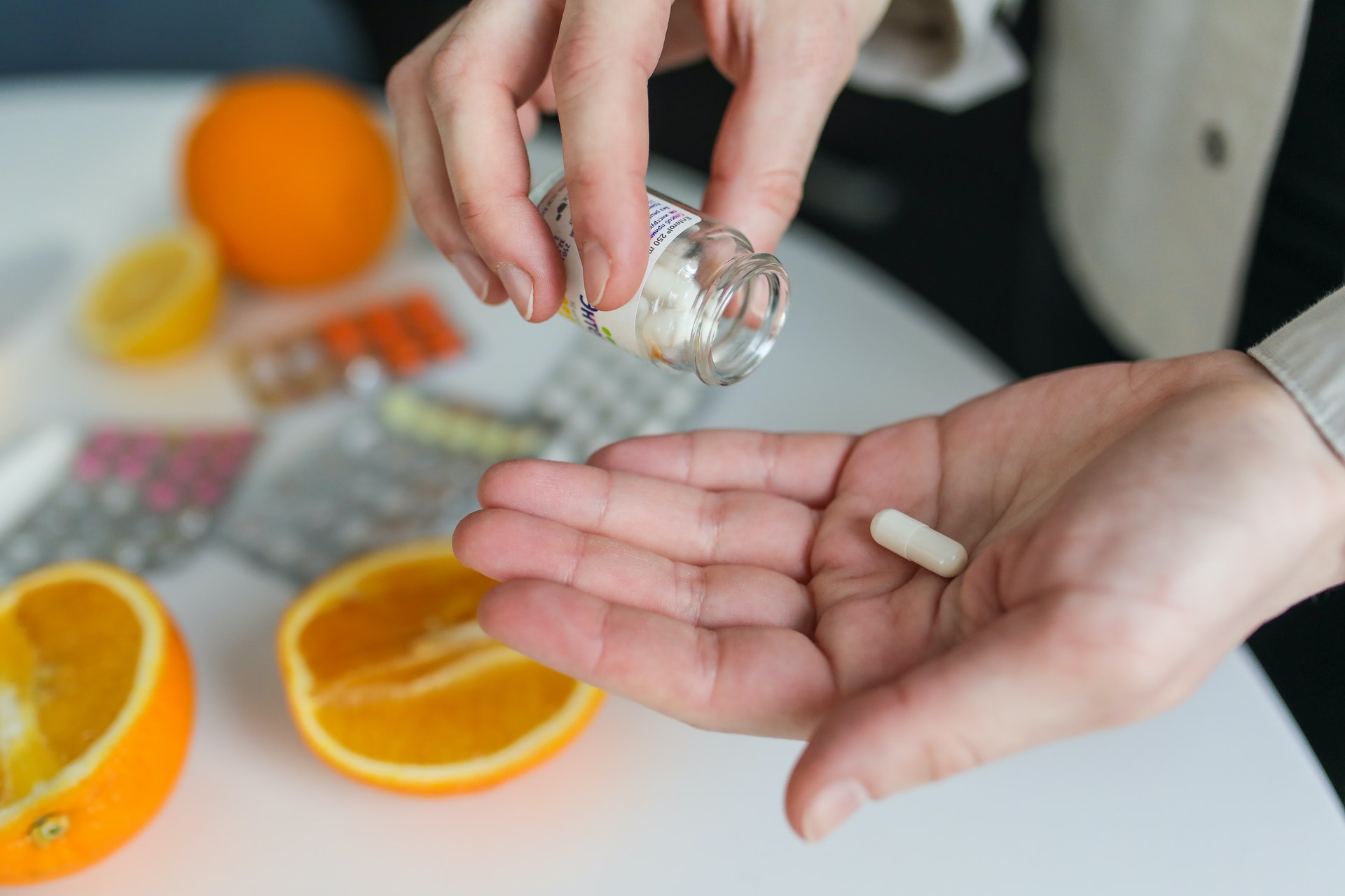 A person's hand holding a pill with orange slices in the background