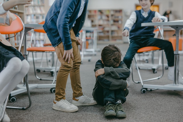 a small child hiding with his arms around his knees while 3 kids point and laugh at him