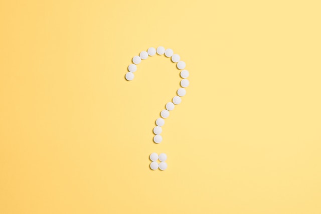 a question mark made out of pills in the shape of a white question mark with a yellow background.