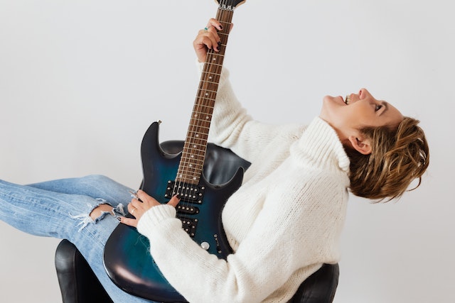 A woman holding an electric guitar, leaning back and smiling