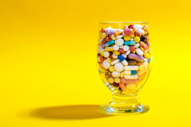 Bright yellow background; a cocktail glass is full of pills like adderall, ritalin, wellbutrin, etc.
