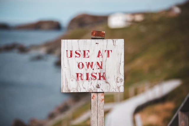 A worn down sign with a beach in the background. The sign reads "use at own risk"