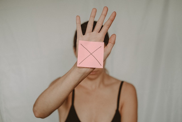 a woman with undiagnosed adhd holding a pink sticky note in front of her face with an x written  on it