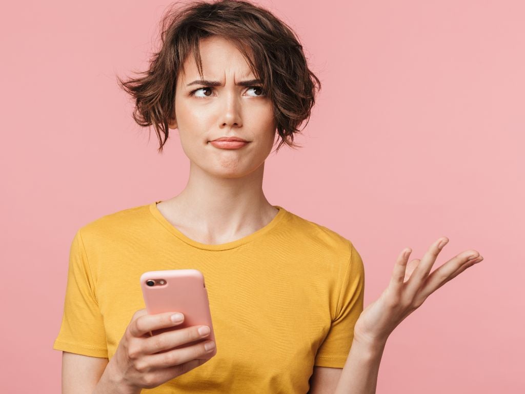 a woman holding a phone with her hand up and a confused expression on her face