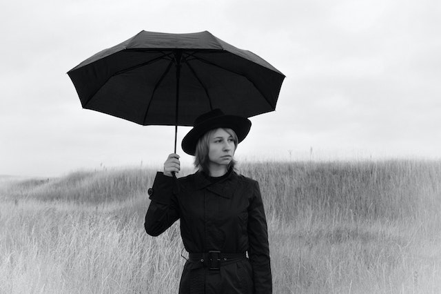 A woman experiencing rejection sensitivity, standing in the rain with an umbrella