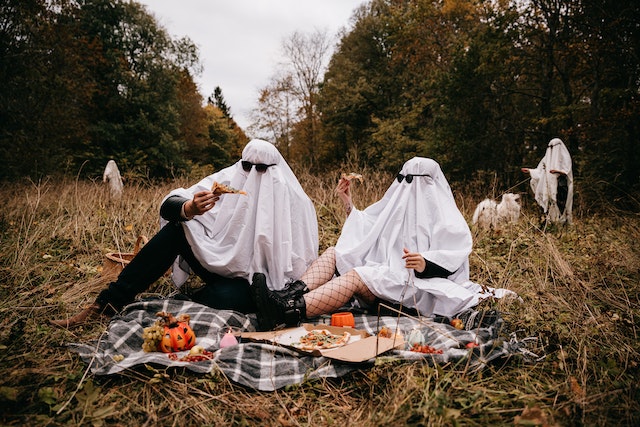 People dressed up as ghosts, having a pizza party in a random field