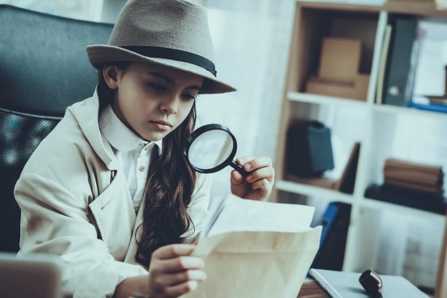a small girls dressed as a detective, holding a magnifying glass up to a paper