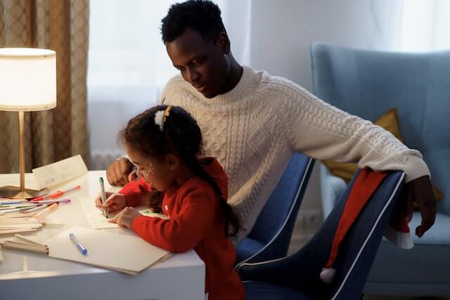 A dad with ADHD helping his daughter work on coloring and writing at a desk.