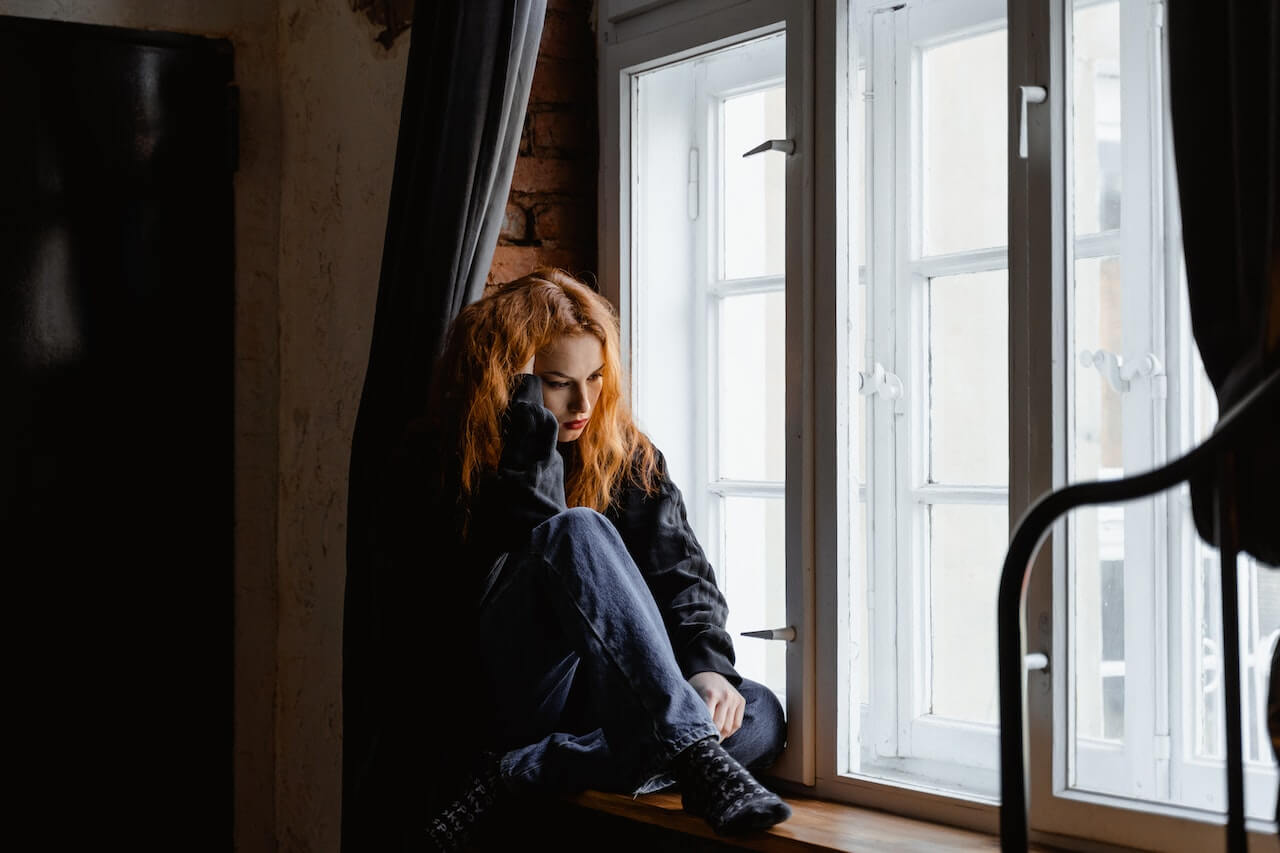 A woman with ADHD and RSD who is sitting by the window and engaging with negative rumination.