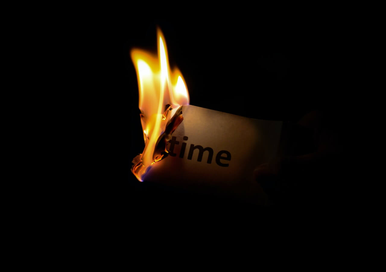 The word "time" is written on a piece of paper and it's on fire in a dark room.
